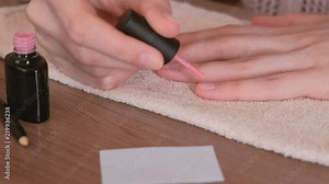 Woman puts first coat of pink shellac on her nails. Close-up.