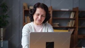 Confident stylish european middle aged senior woman using laptop at home. Stylish older mature 60s lady sitting at table looking at computer screen typing chatting reading writing email