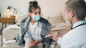 Doctor measuring temperature of young woman in medical mask with thermometer. Male doctor checking temperature to young woman during home visit. Coronavirus protection during the quarantine