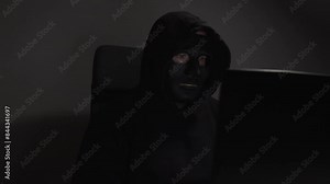 Hacker, man in mask with laptop, hacking into a network, committing cybercrime, accessing sensitive information.
