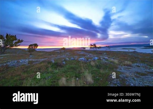 A serene landscape view featuring a vibrant sunset over a calm body of water and rocky terrain Stock Video Footage - Alamy