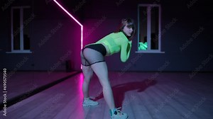 Live camera. Twerk performed by a beautiful young girl in a bright stage costume in a dark choreographic hall with neon lighting