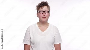 A young woman with short hair, glasses, and lip and nose ring smirks and smiles on a white studio background