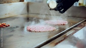 4K Cinematic food cooking footage of a chef preparing and making a delicious homemade burger in a restaurant kitchen in slow motion by seasoning the burgers