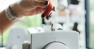 Close-up of the hands of a professional tailor woman. She threads the sewing machine, sets up the spool of thread, and prepares to sew pants for a client. Work process, small business.