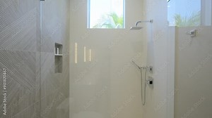 Walk-in shower stall with chrome plumbing, integral shelves for cosmetics and little square window above. Cabinet with transparent glass door and faucet in bathroom