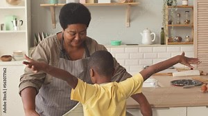 African American grandmother tying apron on her little grandson waist while preparing for cooking and baking at kitchen