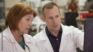 An older female doctor trains a younger male doctor on the hospital computer system.