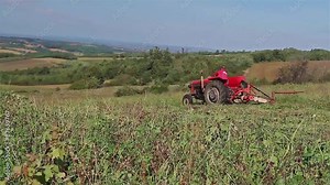 Agricultural activity. Farmer cutting grass with tractor and attached cutter on hilly landscape.