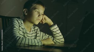 Teenager boy using laptop computer at home at night. Young boy playing computer games, watch video, surf on net