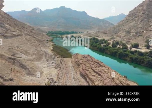 Aerial view of a turquoise river flowing through a rocky desert valley and green palm groves in Oman Stock Video Footage - Alamy