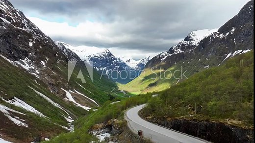 Aerial presenting Hjelledalen valley in Stryn and Norfjord area Norway - Aerial above road with scenic valley and snow capped mountains in background