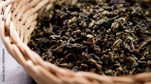 Dry rolled gunpowder green tea leaves in an eco rustic rattan bowl on a board. Healthy herbal drinks. Source of Antioxidants. Rotation