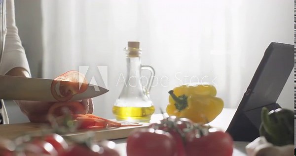 Cooking with app. Woman prepares healthy food at home using checking cookbook app on digital table, slicing tomatoes. Online recipe. Homemade food. Healthy proper nutrition lifestyle