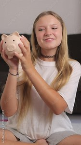 Smiling young teenager girl hold piggy bank, showcasing her enthusiasm for saving and managing finances indoors. Vertical video