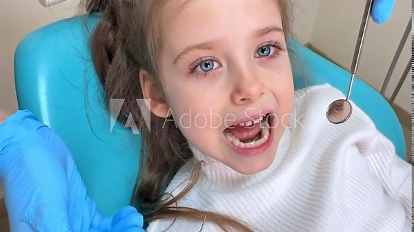 Children dentistry. Hands of unrecognizable pediatric dentist making examination procedure for cute little girl sitting on chair in hospital. Dentist office. Little girl sitting in the dentists office