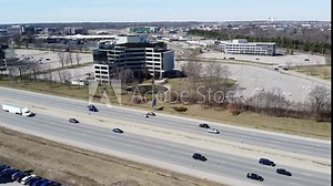 Descending Aerial With Traffic On Interstate By Commercial Buildings City Behind Highway