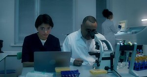 Two people in lab coats looking at a laptop