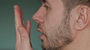 Bad breath from mouth. Close-up of man checking his breath by exhaling into hand