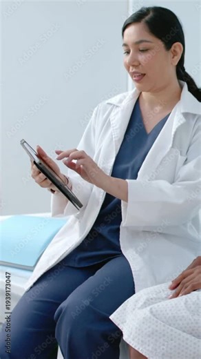 Vertical video: Tapping doctor lab coat using tablet in clinic, showing results to patient in gown