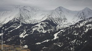 Winter in the Austrian Alps. Fresh snow covers mountain peaks and slopes. Heavy clouds hang above. Arial view. parallax.