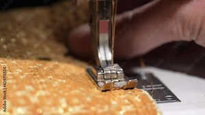 This slow motion close up macro video shows a sewing machine needle going in and out of fabric as it sews.