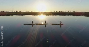 Aerial fly over view of three polers silhouetted against the setting sun rowing their Mokoros on the waterways of the Okavango Delta