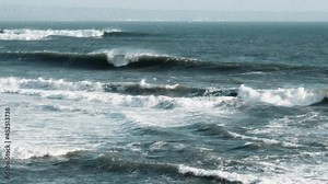 A big strong storm on the ocean in slow motion. The dark green waves of sea rise and collapse with great power, turning into a huge white foam. Seascape with intense sensations and cloudy colors.