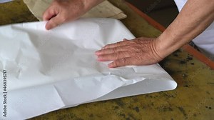 An old calligrapher prepares to fold the rice paper before writing the calligraphy