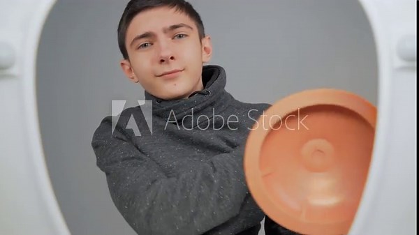 Plumber boy cleaning toilet with plunger. Male teenager using plunger and clean bowl in restroom. View from toilet bottom. Cleanliness and hygiene concept