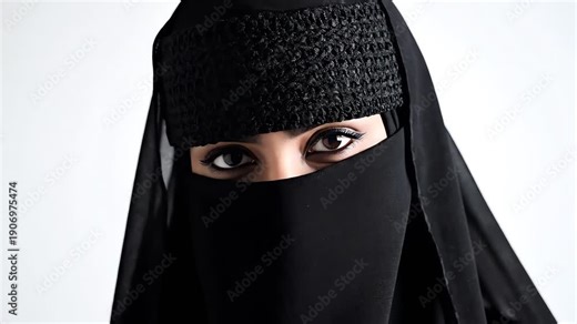 A serious muslim woman wearing a traditional black niqab gazes intensely at the viewer in this high-contrast close-up studio portrait against a plain white background.