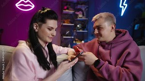 Romantic heterosexual couple texting online. Man and woman send each other SMS, messages, smiling happily, chatting, flirting online through messengers, while sitting side by side on same couch.