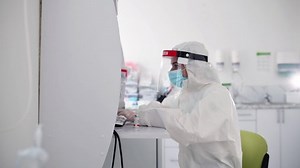 Clinic worker in safety uniform is in the lab with test tubes of COVID-19 vaccine