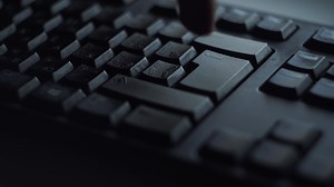 Close-up man presses keyboard key. Man presses button enter computer keyboard. Man's hand presses keyboard in light of computer screen