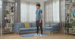 Athletic Fit Asian Man In Sports Clothes Is Doing Jumping Jack Exercises At Home In His Spacious And Bright Apartment