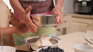 Mother and child sifting flour in kitchen for baking together