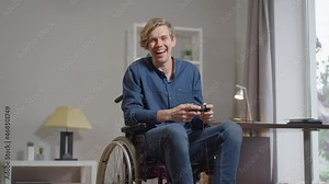 Portrait of joyful Caucasian young handicapped man in wheelchair winning in multiplayer online video game gesturing victory in slow motion. Happy disabled gamer with joystick rejoicing indoors