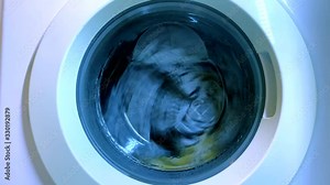 Washing machine washing clothes. Close up view of laundry is washed spinning in washer. Housekeeping and home improvement concept. Drum of the washing machine rotates with sheets