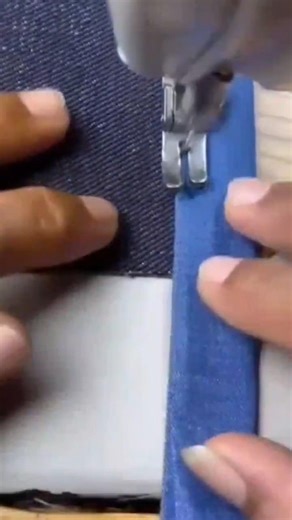 Sewing a blue fabric edge onto a dark textile material using a sewing machine tool