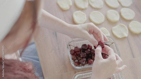 Fresh cherries on dough circles are ready to be baked on a wooden table. Cooking with homemade ingredients requires careful preparation and attention to detail for delicious results
