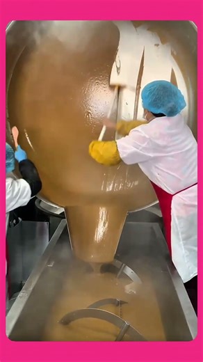 Pouring thick caramel from a giant cooking vat into processing machine in a continuous, smooth flow