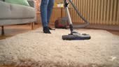 Young woman vacuuming the living room at home. Close up.