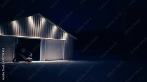 Man Using Snowblowing Machine In Removing Snow Outside Barn At Night. wide shot
