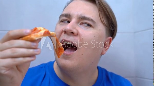 Hand brings slice of thin-crust pepperoni pizza to open mouth, stops, tempts with last piece Man hid in toilet to secretly eat food prohibited on diet, slyly looking sideways, anticipating pleasure