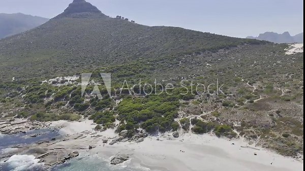 Drone spirals down from view of Mini Lion's Head to Sandy Bay Beach on a sunny morning in Cape Town, South Africa