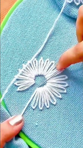embroidering a beautiful white flower pattern precisely on a blue fabric using a thin metal needle