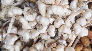 Top view slow motion tracking shot over a pile of many white garlic bulbs on display at a farmers street market.