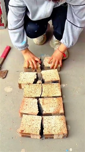 hitting and breaking hard light brown bricks into two pieces using a metal hammer on the ground
