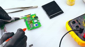 Repair of electronics with the help of a tester.The repair technician tests the electronic board by moving the test leads from one contact on the board to the other. in the frame, only the gloved hand