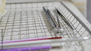 Detailed. Hands of a nurse in gloves put a disinfected dental work tool on a metal grid for autoclaving by ultrasound. DOF, slow motion